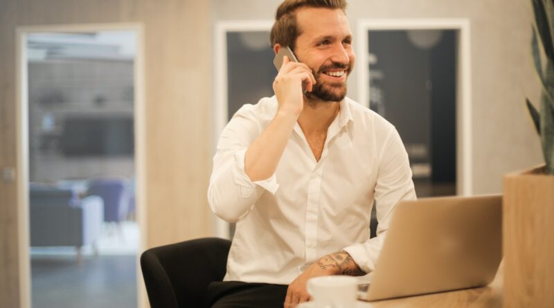 Smiling formal male with laptop chatting via phone