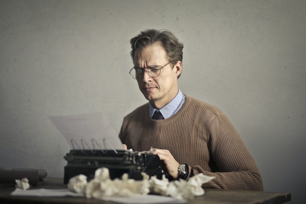 Adult frowned male writer working on typewriter at home
