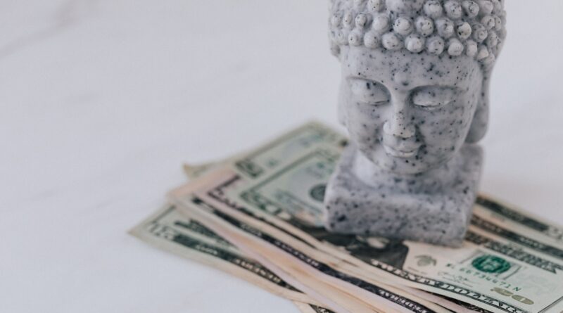 Marble decorative bust of Buddha composed on heap of American dollars on white surface