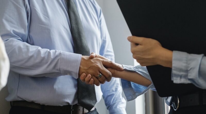 Crop anonymous man in formal shirt and tie shaking hand of woman with black folder while meeting in office