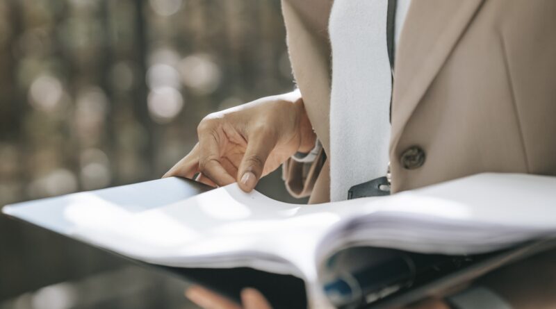 Crop faceless female entrepreneur in stylish jacket reading important documents in black folder