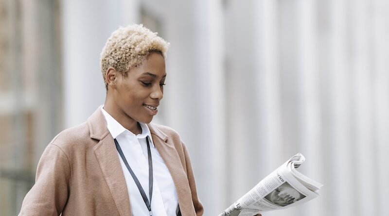 Smiling black businesswoman reading newspaper outside modern building