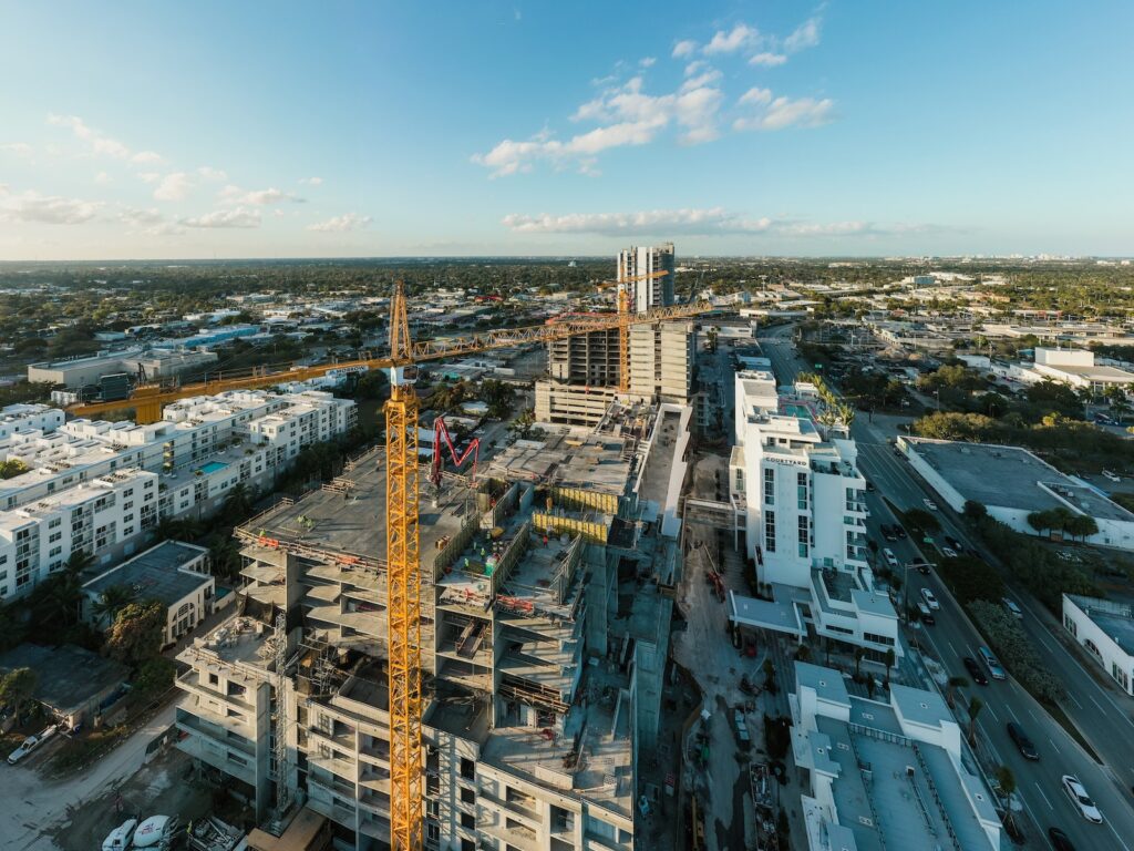 From above of construction site with tower crane in residential district of modern city against cloudy blue sky