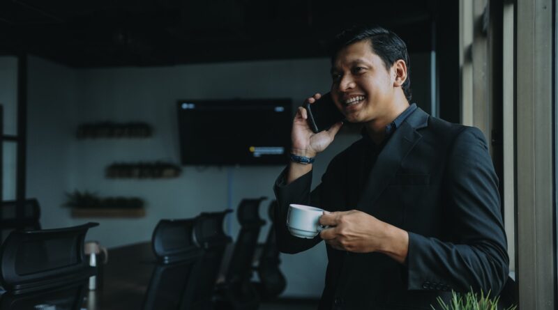 smiling man holding cup and using smartphone