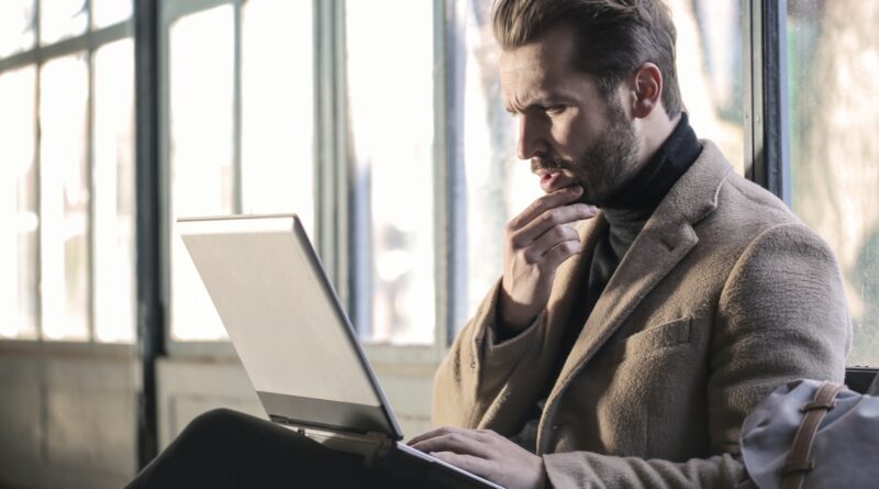 Man Wearing Brown Jacket and Using Grey Laptop