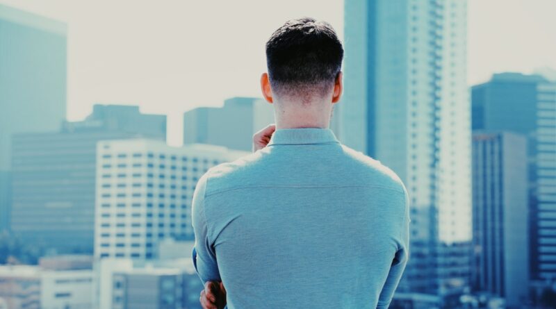 man in blue long sleeve shirt standing in front of city buildings during daytime
