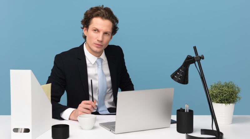 man sitting on chair beside laptop computer and teacup