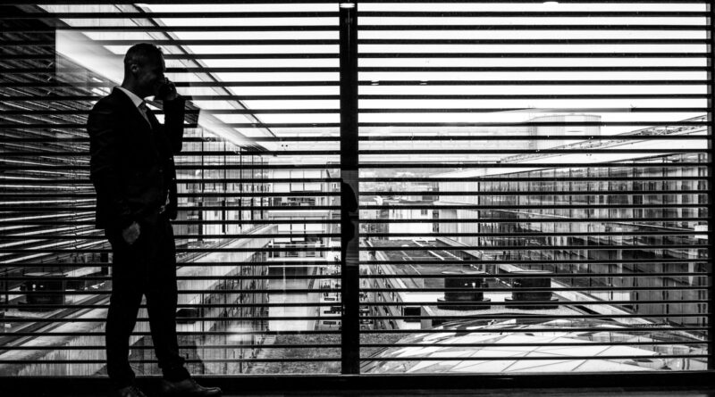 silhouette of man standing beside clear glass wall while using smartphone