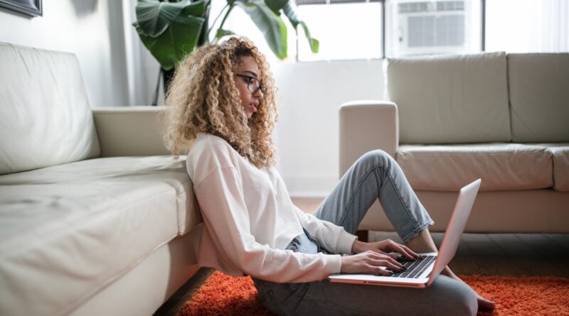 woman sitting on floor and leaning on couch using laptop